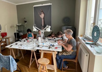 Art Clay ékszerkészítő workshop Budapesten. a háttérben egy üvegékszerről készült plakáttal.